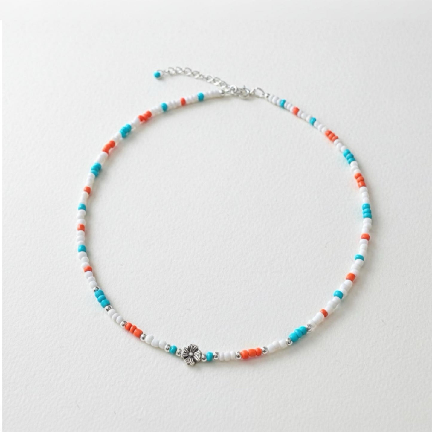 Schmale Perlenkette bunt Echt Silber mit Blumenperle in Türkis, Orange und Weiß auf einem neutralen Hintergrund.