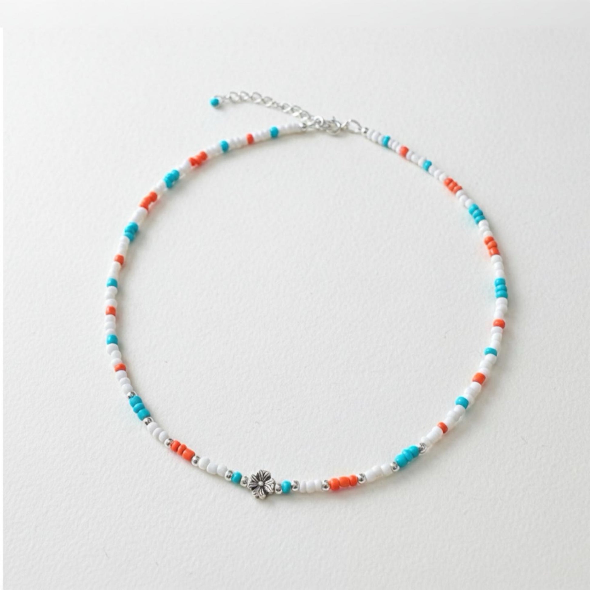 Schmale Perlenkette bunt Echt Silber mit Blumenperle in Türkis, Orange und Weiß auf einem neutralen Hintergrund.