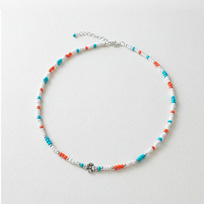 Schmale Perlenkette bunt Echt Silber mit Blumenperle in Türkis, Orange und Weiß auf einem neutralen Hintergrund.