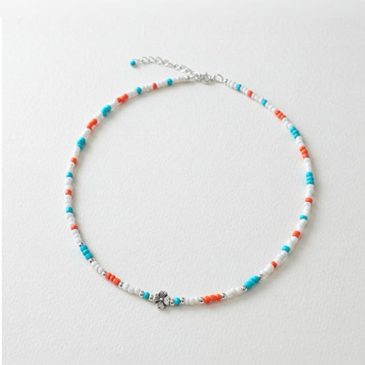 Schmale Perlenkette bunt Echt Silber mit Blumenperle in Türkis, Orange und Weiß auf einem neutralen Hintergrund.